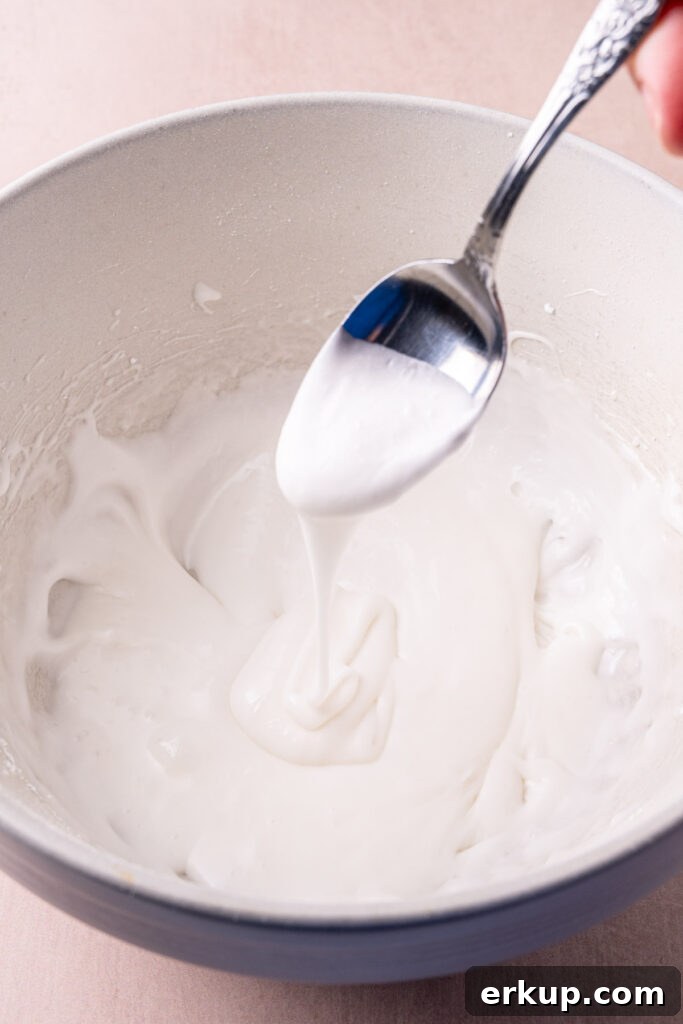Silky Pourable Coconut Glaze for Cakes and Pastries 5 Letting coconut glaze run off a spoon to assess the consistency to know whether or not to add more coconut milk.