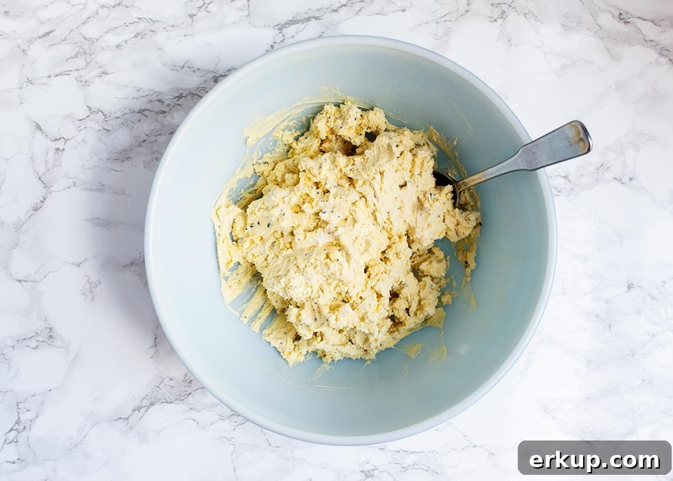 Keto Deviled Eggs with Everything Bagel Seasoning Recipe 6 overhead view of keto deviled eggs mixture in a blue bowl with a spoon sticking out of the right side