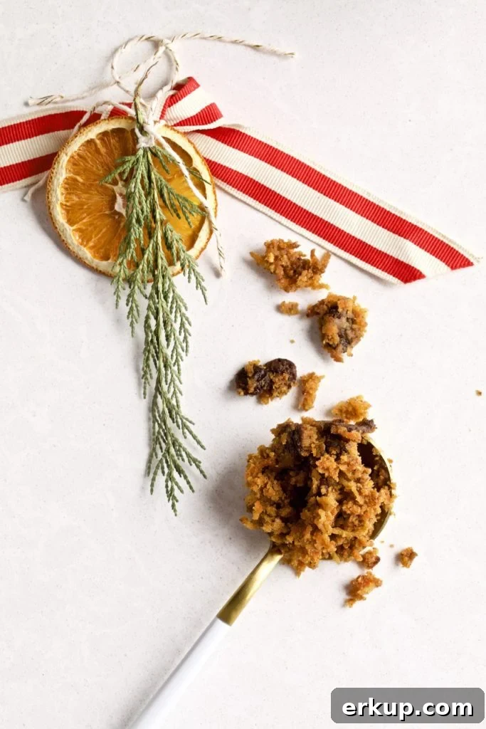 Steamed carrot pudding on a spoon next to a sprig with an orange slice and ribbon.