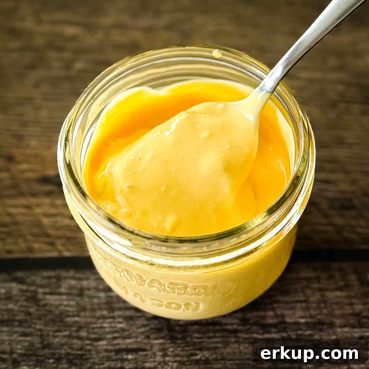 A spoon scooping up some creamy smashburger sauce from a glass jar.