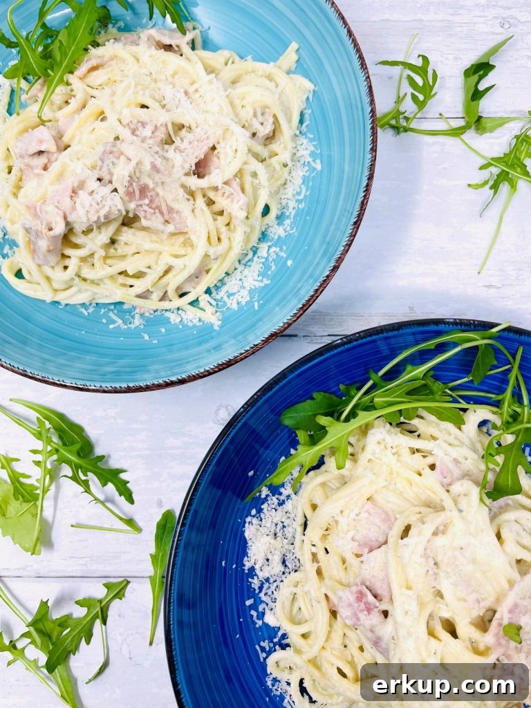 Two bowls of creamy bacon pasta topped with rocket and cheese