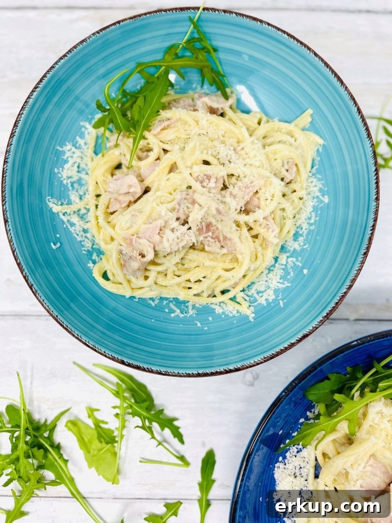 Two bowls of creamy bacon pasta topped with rocket and cheese