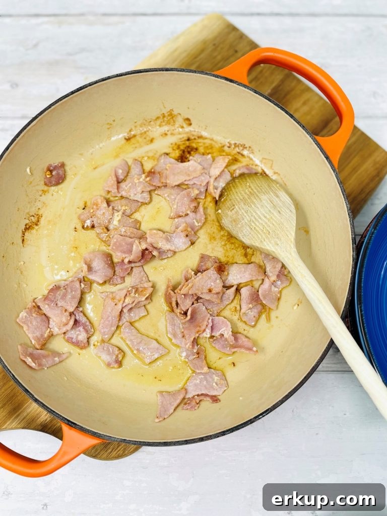 Orange pan with bacon in being mixed with a wooden spoon