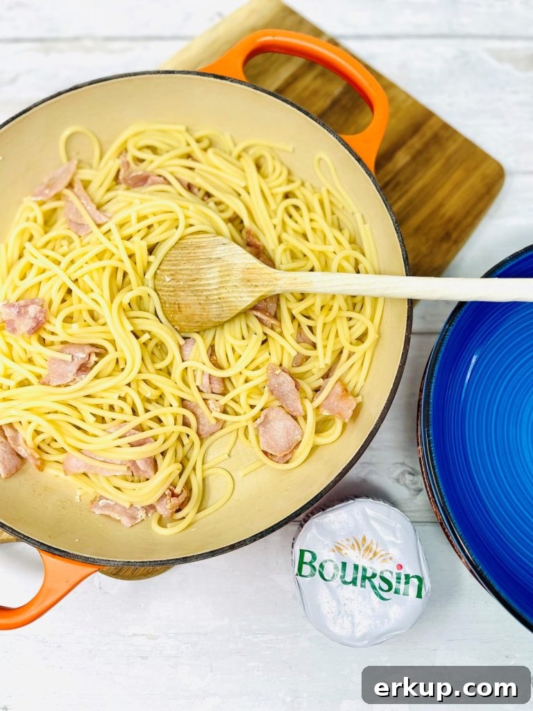 Bacon and spaghetti in a pan being mixed by a wooden spoon
