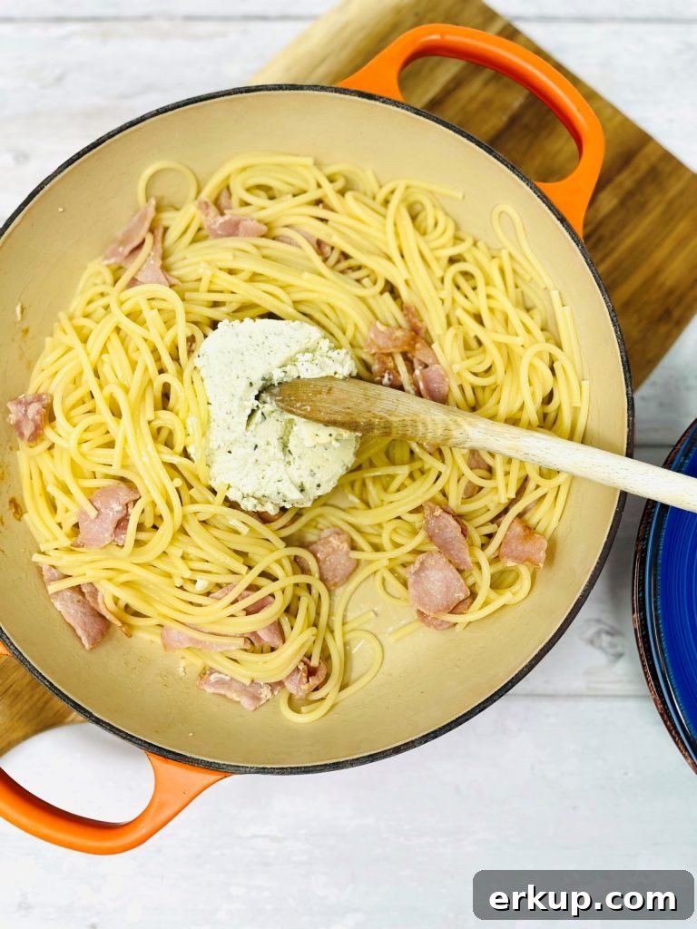 Bacon and spaghetti and boursin in a pan being mixed by a wooden spoon