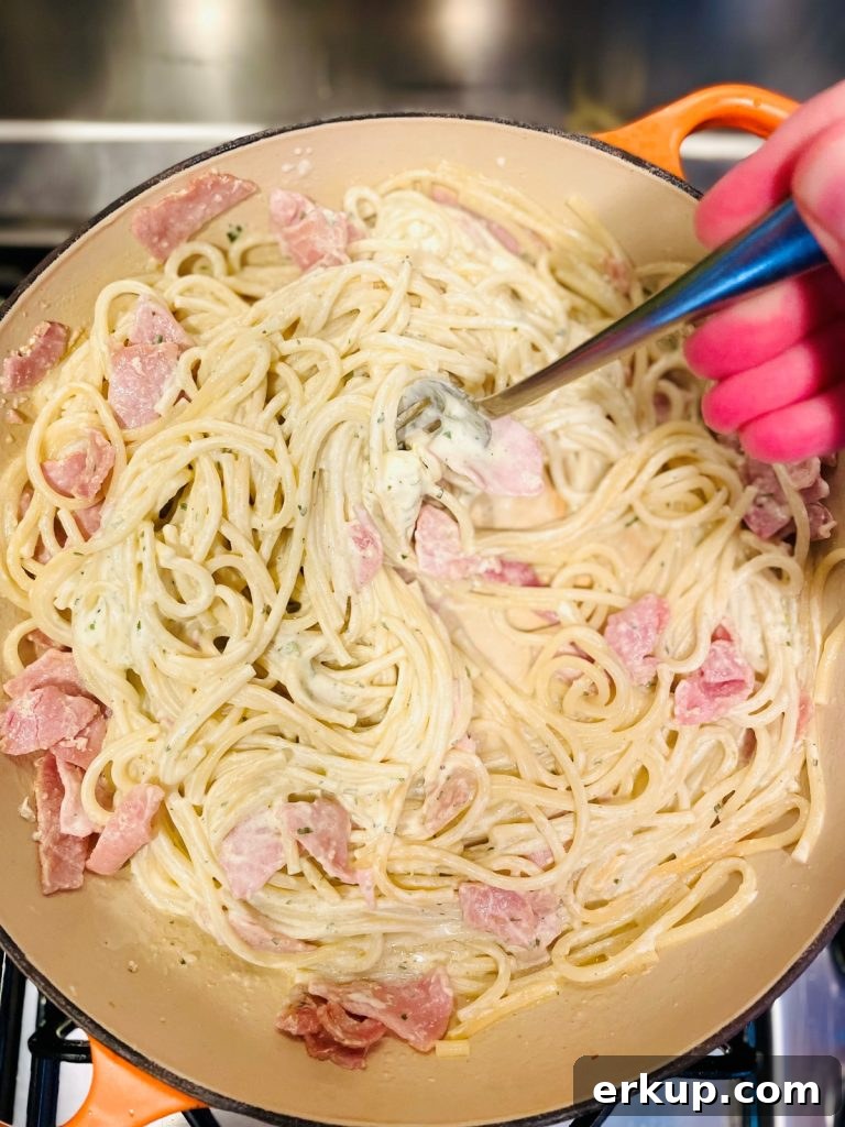 Creamy bacon pasta being mixed in a pan with a metal fork