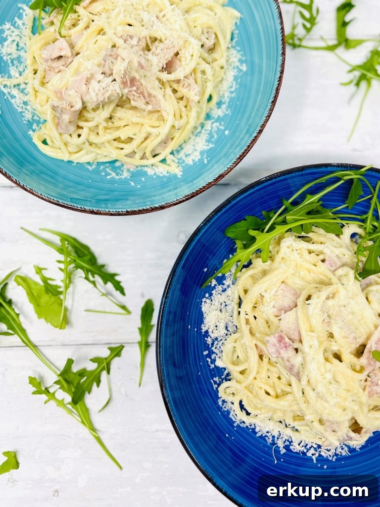 Two bowls of creamy bacon pasta topped with rocket and cheese