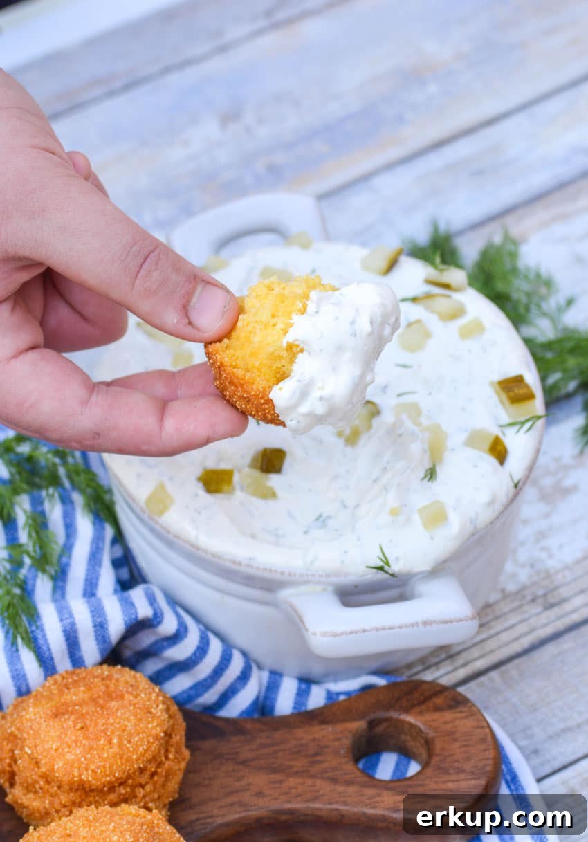 a broken hush puppie dipped in a bowl of pickle dip