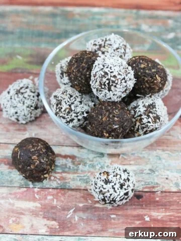 Chocolate coconut energy balls with dates in a glass bowl with three energy balls beside the bowl and coconut around it.