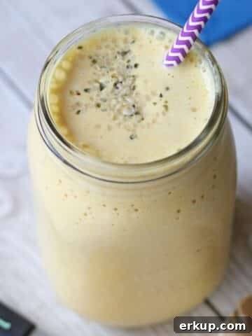 Turmeric peach smoothie in a mason jar with a purple straw. Turmeric root and powder and ginger root around it.