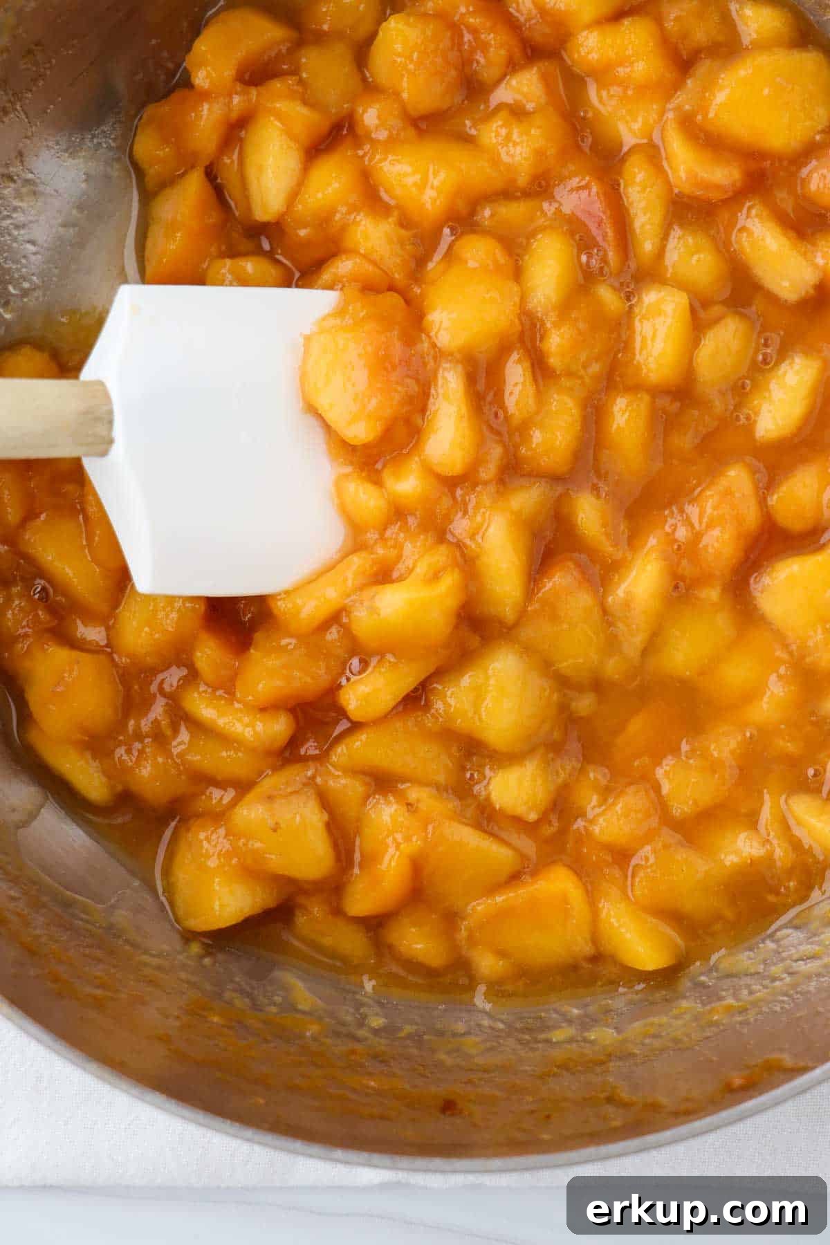 Peach compote in a saucepan with a rubber spatula.