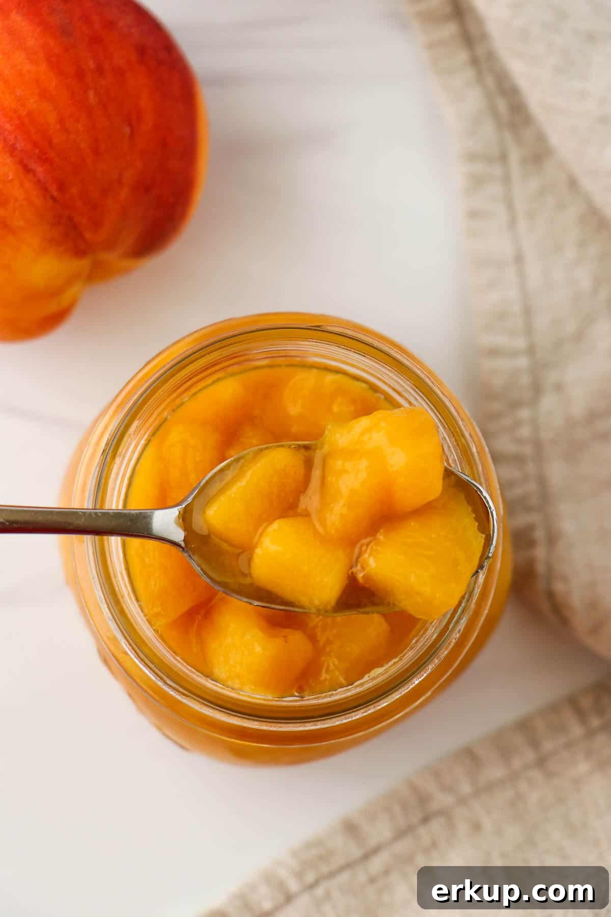 Overhead shot of peach compote on a spoon next to a peach.