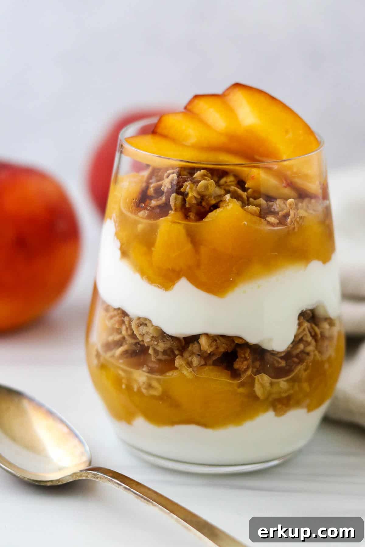Yogurt and granola parfait layered with peach compote next to a spoon.