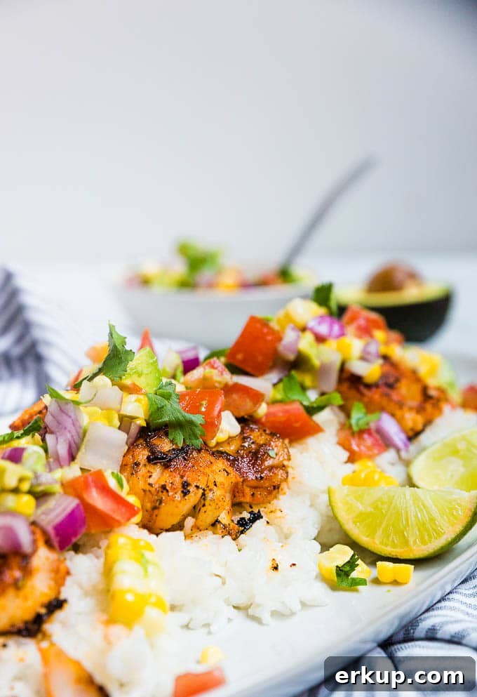 A plate of cod with blackened spices and tomato avocado corn salsa with lime.