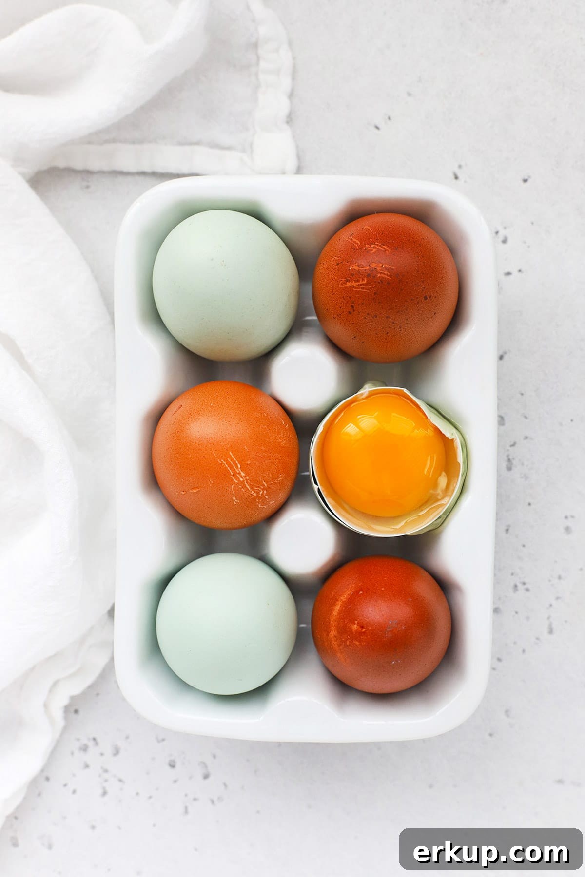 Overhead view of an egg carton with 6 eggs. One egg is open, revealing a golden yolk