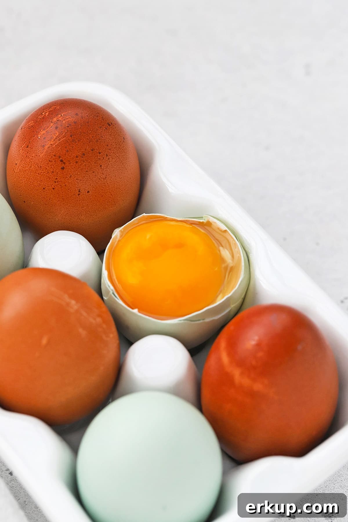 Front view of an egg carton with 6 eggs. One egg is open, revealing a golden yolk