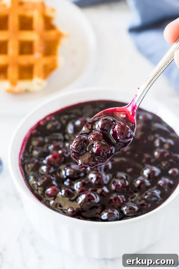 A bowl of homemade blueberry sauce with a spoon taking some out of the bowl.