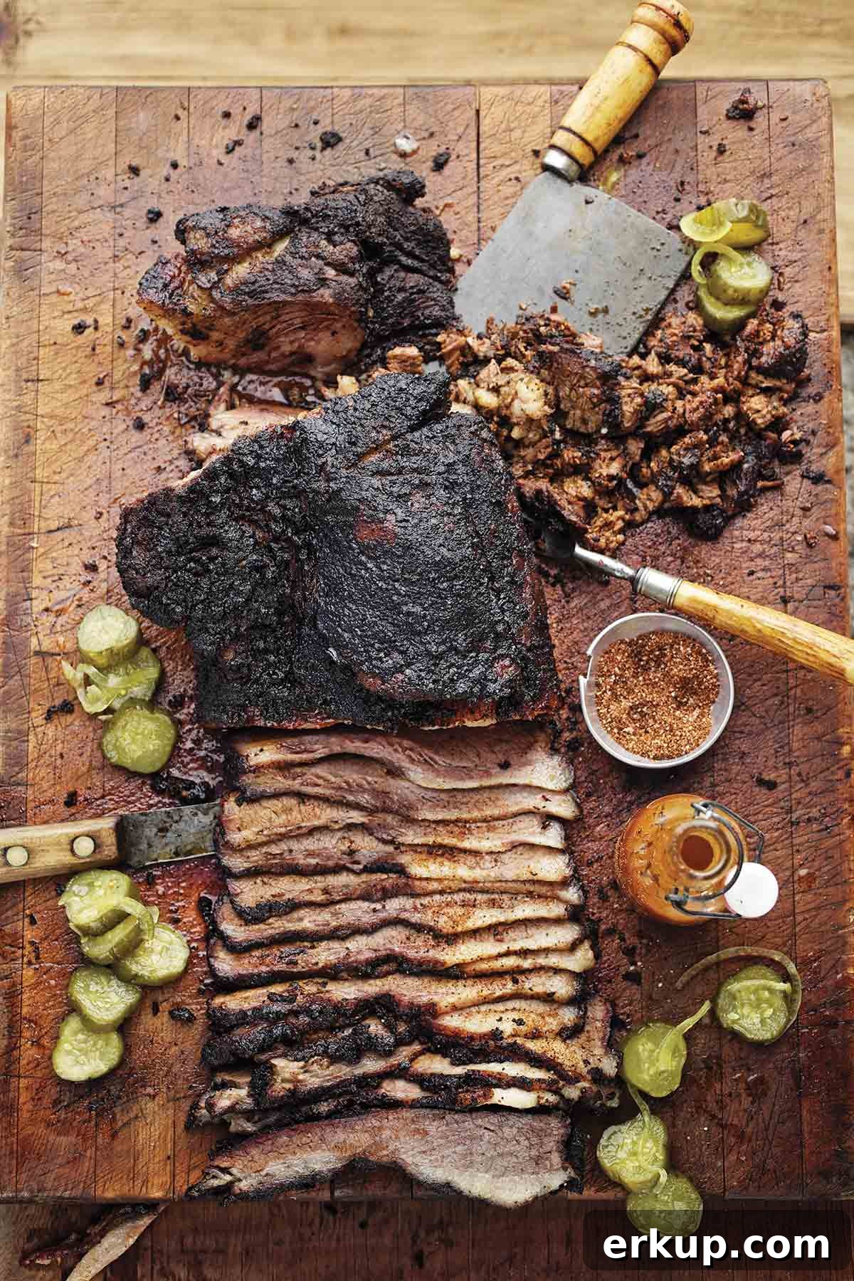 Smoked Barbecue Beef Brisket Recipe for Tender, Juicy Results 2 A partially sliced barbecue beef brisket on a cutting board with spice rub, hot sauce, and pickle slices scattered around it.