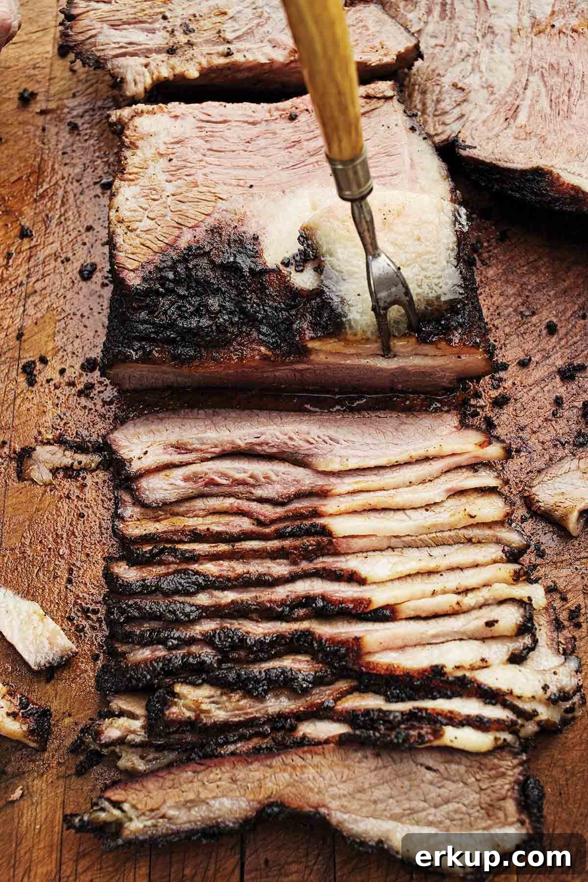 Smoked Barbecue Beef Brisket Recipe for Tender, Juicy Results 3 A partially sliced barbecue beef brisket on a cutting board with a meat fork poking it.
