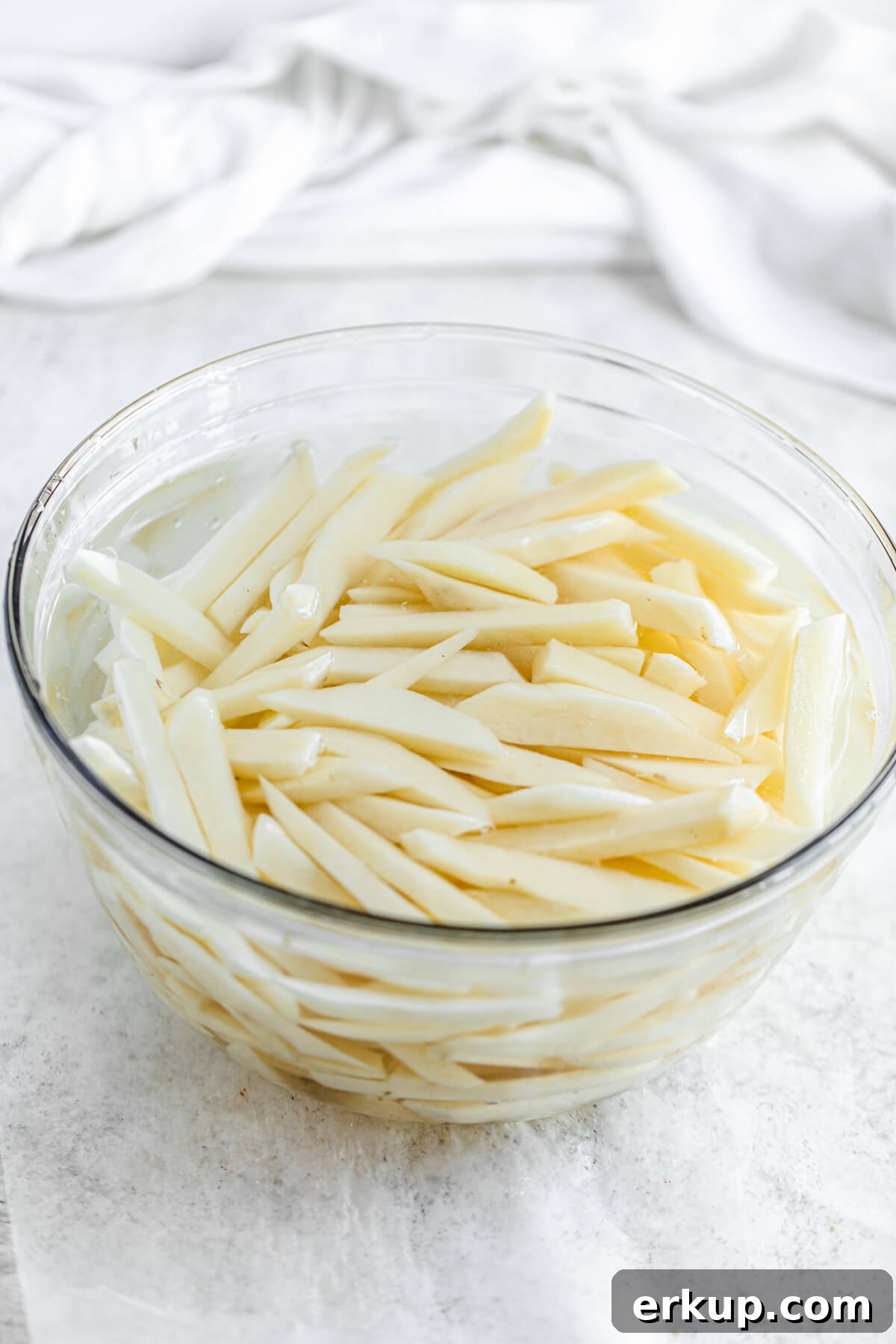 potato French fry sticks in a large glass bowl of cold water