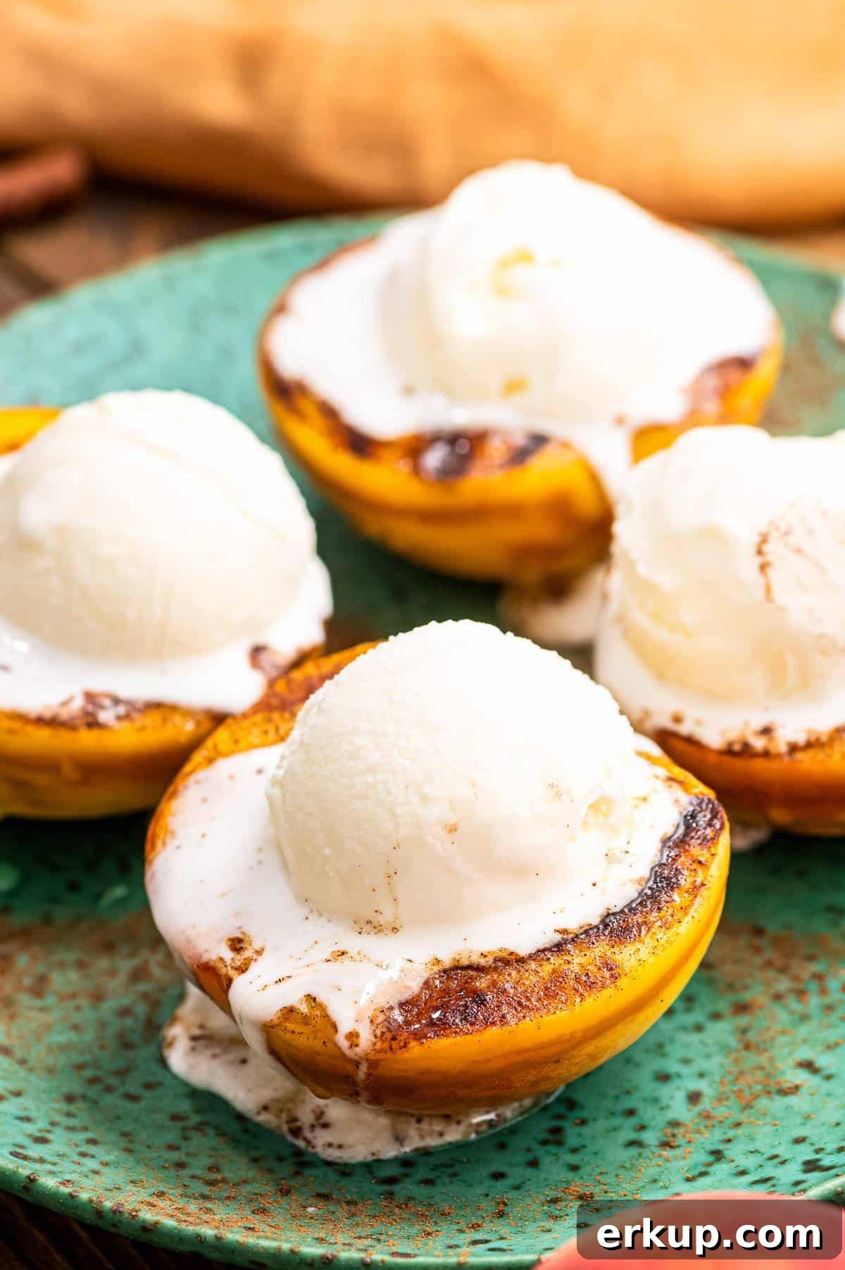 Close up image of four peaches halves that are grilled with a scoop of ice cream on top.