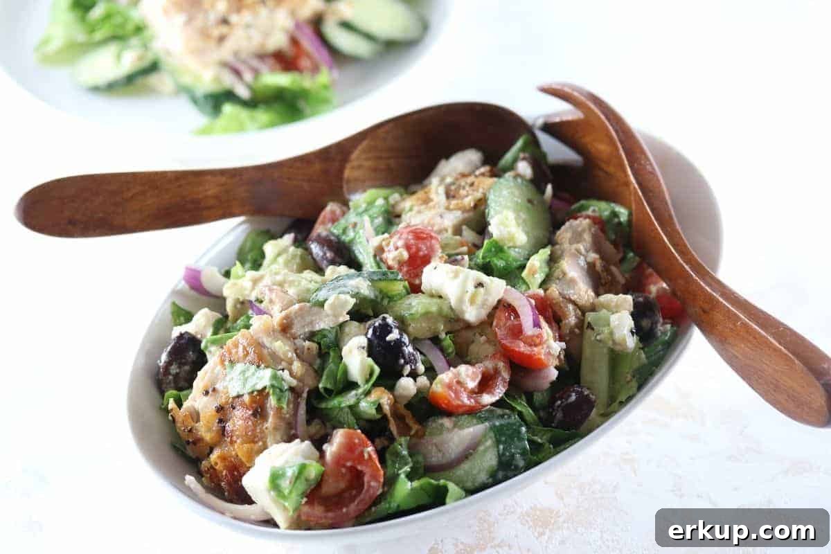 Oval bowl filled with Chicken Mediterranean Salad Recipe with wooden salad servers on the side.