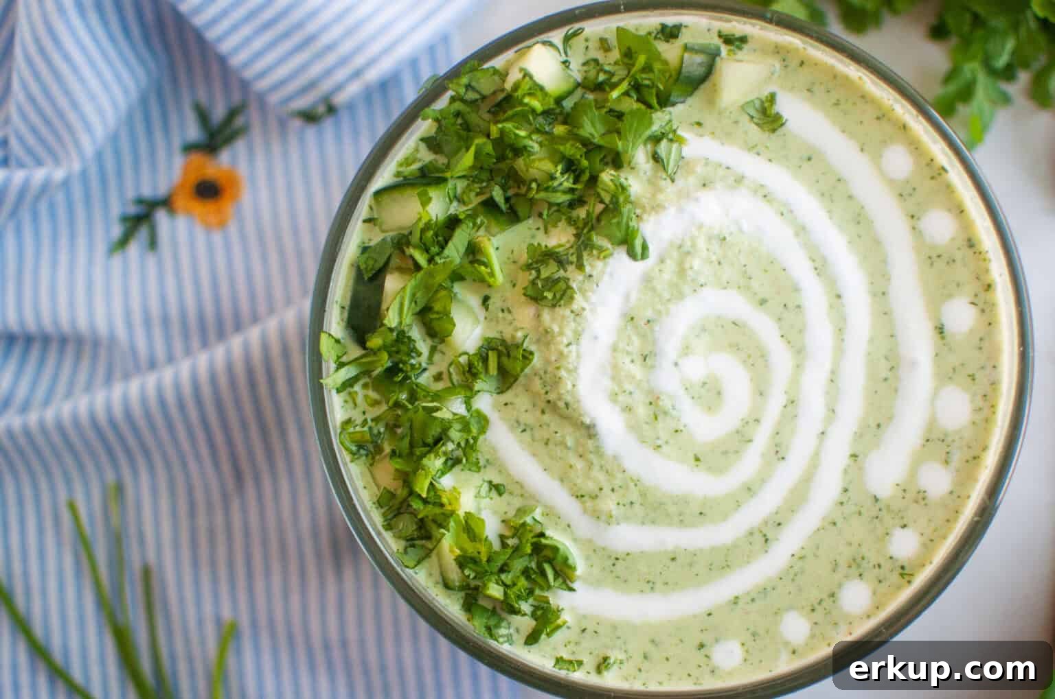 A bowl of Low-Carb Cool & Creamy Cucumber Gazpacho on a blue and white striped cloth.