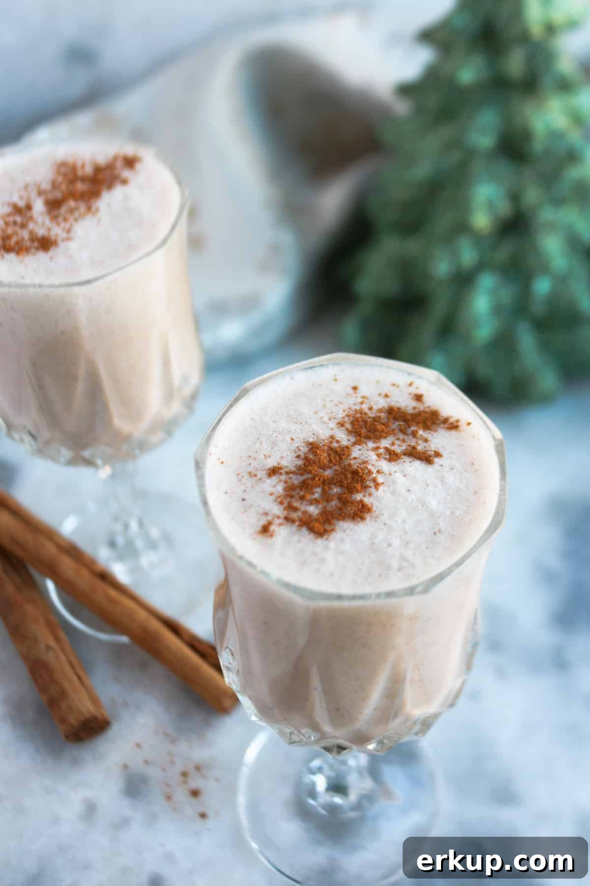 Creamy Vegan Coquito Recipe for the Holidays 6 Two clear glasses with Puerto Rican coquito sprinkled with cinnamon powder, with two cinnamon sticks beside them.